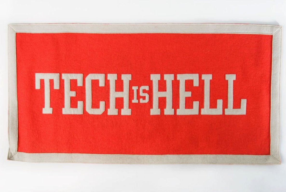 A red felt banner with white block letters that read Tech is Hell